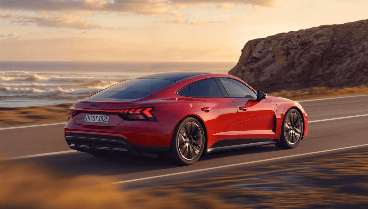 Audi e-tron GT rouge sur route côtière au coucher du soleil